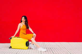 女人坐着前黄色的手提箱前面红色的墙女人坐着前黄色的手提箱前面红色的墙
