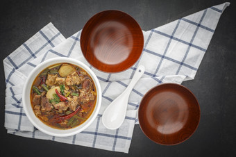 汤姆百胜泰国食物热辣的和酸红烧牛肉汤碗与白色陶瓷勺子空木碗和表格餐巾黑暗灰色的灰色黑色的语气纹理背景