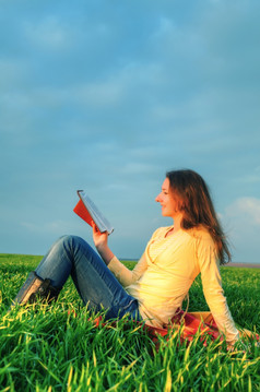 青少年女孩阅读的圣经坐着在户外日落时间