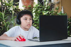 亚洲男孩穿无线耳机和使用移动PC电脑研究在线和搜索的互联网