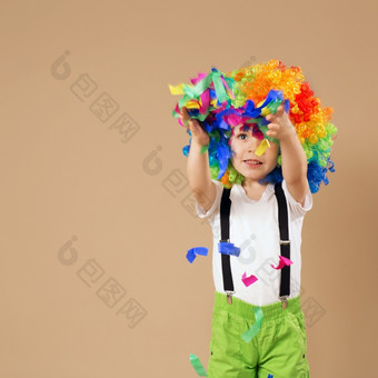 快乐小丑男孩与大色彩斑斓的假发小男孩小丑假发跳和有有趣的肖像孩子抛出多色的俗丽的和五彩纸屑生日男孩