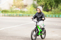 肖像可爱的小城市男孩穿黑色的皮革夹克城市风格城市孩子们的男孩学习骑自行车孩子开车自行车
