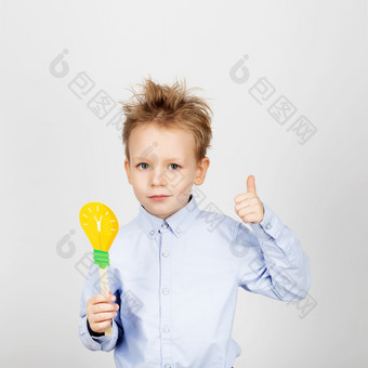 可爱的男孩与黄色的纸灯泡对白色背景小学生手势拇指持有玩具灯泡快乐的微笑孩子与有趣的照片道具学校概念回来学校