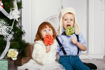 小孩子们吃<strong>棒棒糖</strong>肖像两个有趣的小孩子们与美味的糖果的手快乐孩子们和家庭期待新一年和圣诞节