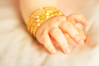 婴儿手婴儿手与黄色的黄金手镯孤立的对白色丝绸