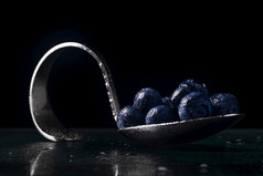 弯曲的铬勺子与蓝莓与滴水黑暗背景