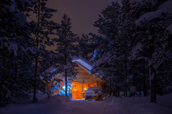 冬天无风的晚上密集的云杉森林木房子点燃和很多雪车和雪地是在那里房子的森林晚上