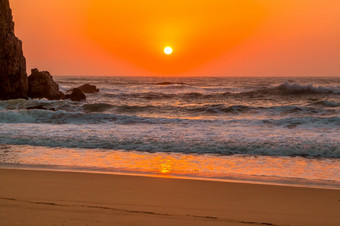的桑迪海滩葡萄牙日落岩石波和明亮的太阳纯橙色天空橙色日落的葡萄牙语海滩