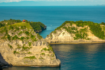 印尼岩石海岸热带岛小房子前的山郁郁葱葱的植被和绿松石海洋水岩石热带海岸和小房子前