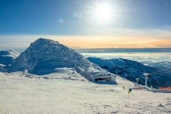 冬天山白雪覆盖的山峰和雾的山谷明亮的太阳的蓝色的天空在的滑雪运行滑雪电梯和酒吧冬天太阳在的山峰和滑雪酒吧