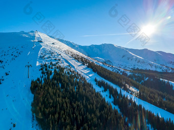 冬天斯洛伐克滑雪度假胜地明亮阳光明媚的天气滑雪山坡上的树木繁茂的山的太阳照明亮的蓝色的天空空中视图滑雪山坡上的度假胜地和的太阳空中视图