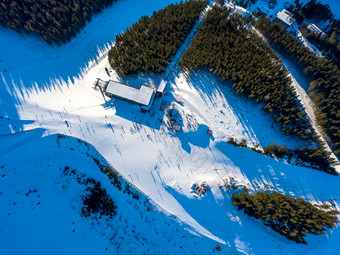 滑雪度假胜地阳光明媚的天气滑雪坡树木繁茂的山许多游客附近的滑雪电梯站和咖啡馆空中视图滑雪电梯站和咖啡馆空中视图垂直下来