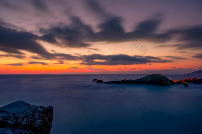 岩石海岸的海色彩斑斓的日落的天空与云色彩斑斓的日落附近沿海石头