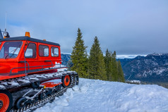 多云的天空在白雪覆盖的山山峰树木繁茂的山坡上红色的雪地履带式车辆的前景红色的雪地履带式车辆和多云的天空在冬天山