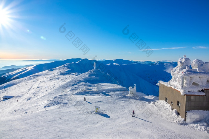 太阳的蓝色的天空在的冬天山山峰冰雪覆盖的建筑的上滑雪电梯站冬天山峰和的建筑的上电梯站