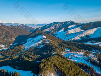 冬天斯洛伐克蓝色的天空阳光明媚的一天的明亮滑雪度假胜地山山峰和滑雪山坡上空中视图冬天山山峰和谷滑雪度假胜地阳光明媚的一天空中视图