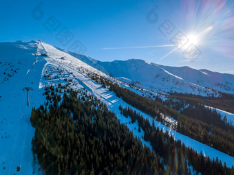 斯洛伐克明亮阳光明媚的冬天天气滑雪山坡上的树木繁茂的山的太阳照明亮的蓝色的天空空中视图太阳和山坡上的滑雪度假胜地空中视图