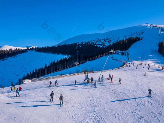 斯洛伐克冬天明亮阳光明媚的一天滑雪山坡上的树木繁茂的山太阳照明亮和蓝色的天空空中视图滑雪者的滑雪坡阳光明媚的冬天一天空中视图