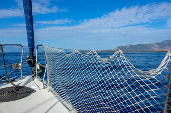 航行游艇的平静海附近丘陵海岸游艇弓绳子和云的蓝色的天空弓航行游艇和海海岸