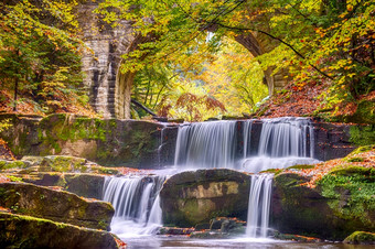 秋天一天的阳光明媚的森林老石头桥小河和几个自然瀑布河瀑布的森林和拱石头桥