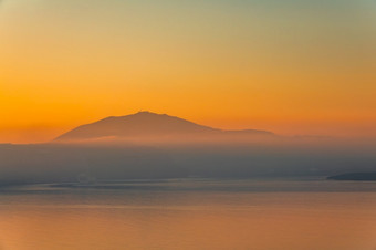 的平静表面的海后日落橙色天空和雾在的多山的海岸晚上雾在多山的海岸