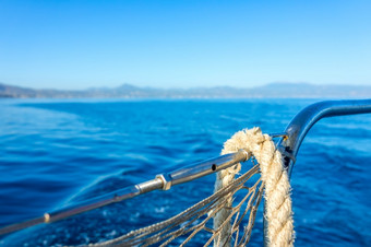 阳光明媚的夏天一天的海湾船尾栏杆航行游艇的老绳子挂起的铁路老绳子的斯特恩栏杆航行游艇