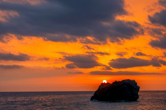 日落在孤独的岩石平静海令人惊异的颜色的多云的天空令人惊异的颜色海日落和孤独的岩石