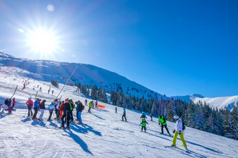 斯洛伐克冬天明亮阳光明媚的一天几个成人滑雪者和孩子们的滑雪坡的树木繁茂的山的太阳照明亮和的蓝色的天空成年人滑雪者和孩子们的滑雪坡阳光明媚的冬天一天