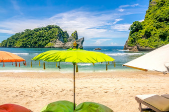 印尼小桑迪海滩热带岛雨伞和日光浴浴床的前景海洋和岩石胰岛的背景没有人雨伞和日光浴浴床热带海滩