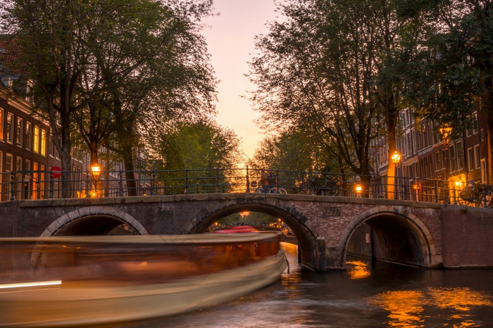 荷兰安静的日落的阿姆斯特丹运河快乐船下的石头桥日落的阿姆斯特丹运河和船下的桥
