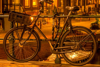 荷兰晚上阿姆斯特丹自行车与行李篮子停的运河栅栏和担保与防盗链停自行车阿姆斯特丹晚上