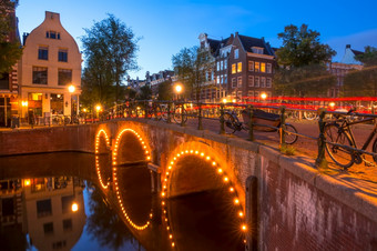荷兰石头桥与三个拱门的阿姆斯特丹运河很多停自行车结束的晚上结束的晚上的阿姆斯特丹桥