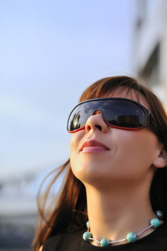 有吸引力的年轻的女人穿太阳镜蓝色的天空背景