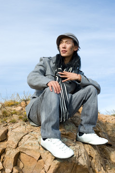 年轻的亚洲男人。灰色外套而且条纹黑白围巾坐在岩石的窗饰他的脸颊他的的名字Chinghis古老的蒙古