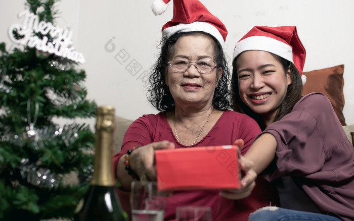 两个老妈妈。和女儿穿圣诞老人他拥抱和持有礼物首页与模糊前景树和瓶圣诞节新一年庆祝活动概念