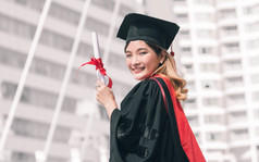 肖像女学生穿统一的和帽毕业她持有证书和微笑与成功幸福骄傲教育概念