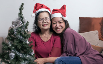 两个<strong>老妈妈</strong>。和女儿穿圣诞<strong>老</strong>人他拥抱和坐着生活房间首页与模糊前景树和瓶圣诞节新一年庆祝活动概念