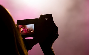 轮廓手持有相机取照片乐队音乐会与色彩斑斓的光