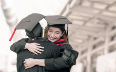 两个亚洲女学生穿统一的帽和微笑拥抱每一个其他与幸福后毕业教育概念