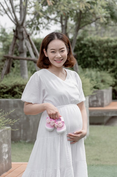 亚洲到美丽的妈妈。持有粉红色的女孩rsquo鞋子而站花园