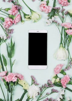 空白智能手机包围与新鲜的limonium康乃馨eustoma花对蓝色的背景