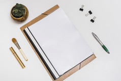 空白螺旋笔记本与使刷睫毛膏纸剪辑笔与盆栽植物白色桌子上