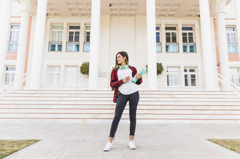 肖像微笑十几岁的女学生持有书外卖咖啡杯站前面<strong>大学建筑</strong>