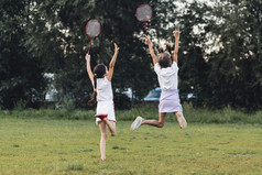 后视图两个女孩跳公园持有羽毛球