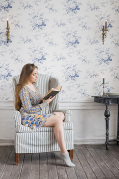 年轻的女人坐着手臂椅子对壁纸阅读书