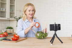 高级女人使视频调用移动电话显示贝尔胡椒片而准备沙拉