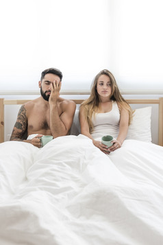 年轻的夫妇与杯咖啡坐着床上