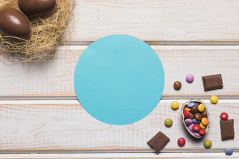 蓝色的圆形框架与巧克力复活节鸡蛋巢木桌子上