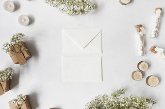 两个信封包围与婴儿呼吸花蜡烛棉花糖测试管微型树树桩礼物盒子白色背景