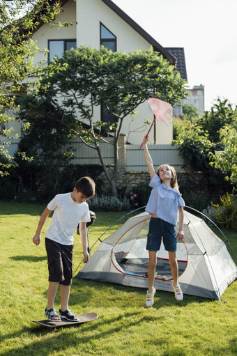女孩捕捉蝴蝶与独家新闻网男孩玩滑板附近帐篷营